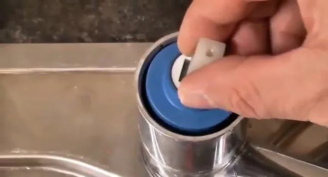 Fingers lifting a blue cartridge out of a chrome mixer tap body