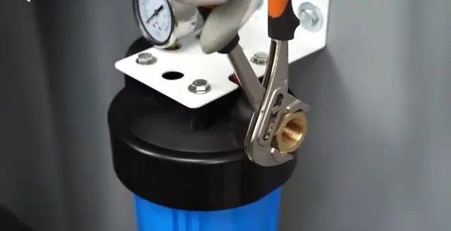 Blue filter housing on a wall bracket with pliers on the brass fitting