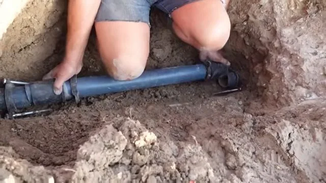 Person kneeling in a trench laying a length of blue pipe