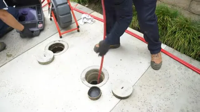 Technician feeding a red cable into a drain pit on a concrete pad with a camera unit beside it