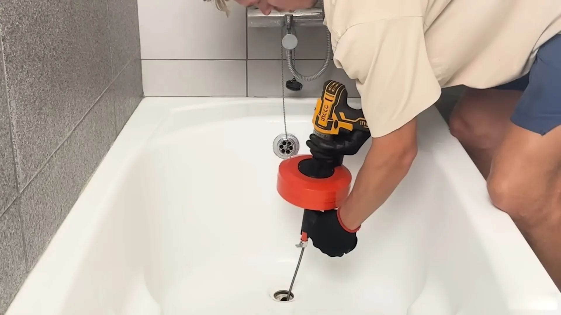 Technician using a powered drain auger in a white bathtub