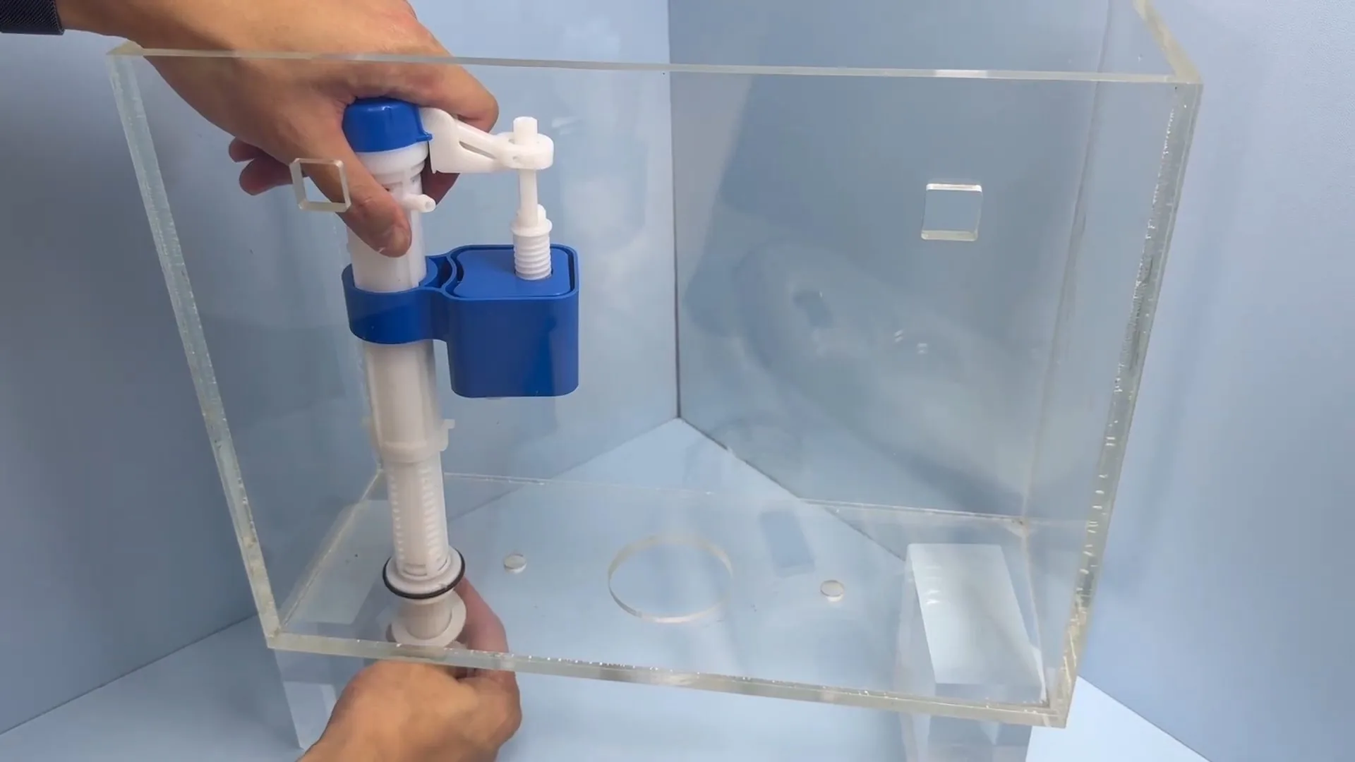 Hands adjusting a float-type fill valve inside a clear demonstration toilet cistern