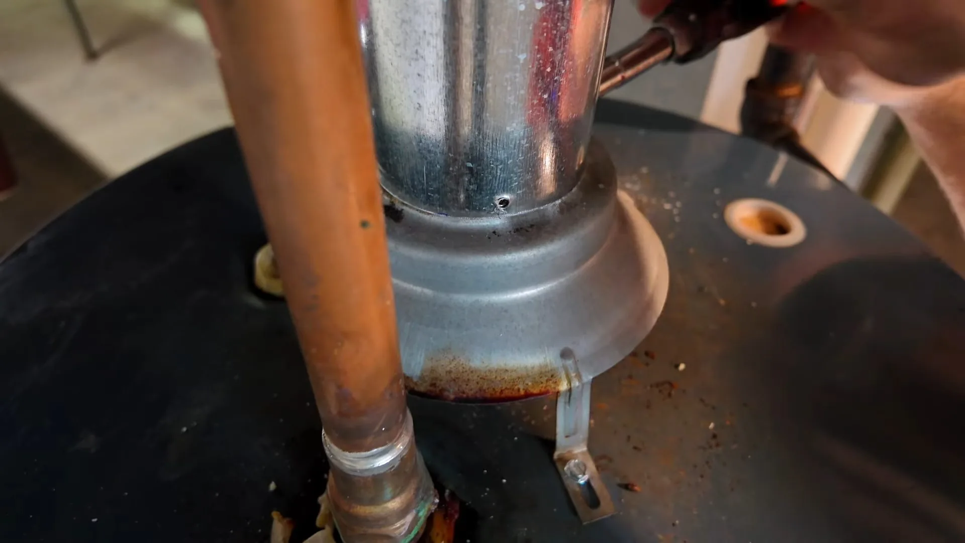 Close view of a galvanised flue collar and a copper pipe rising from the top of a black water heater tank