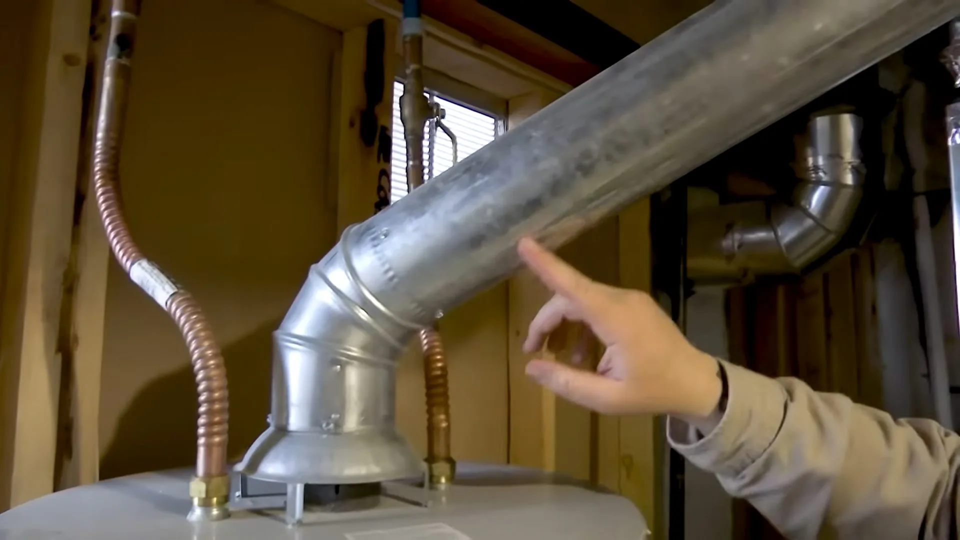 Hand pointing at a metal flue pipe rising from a gas water heater