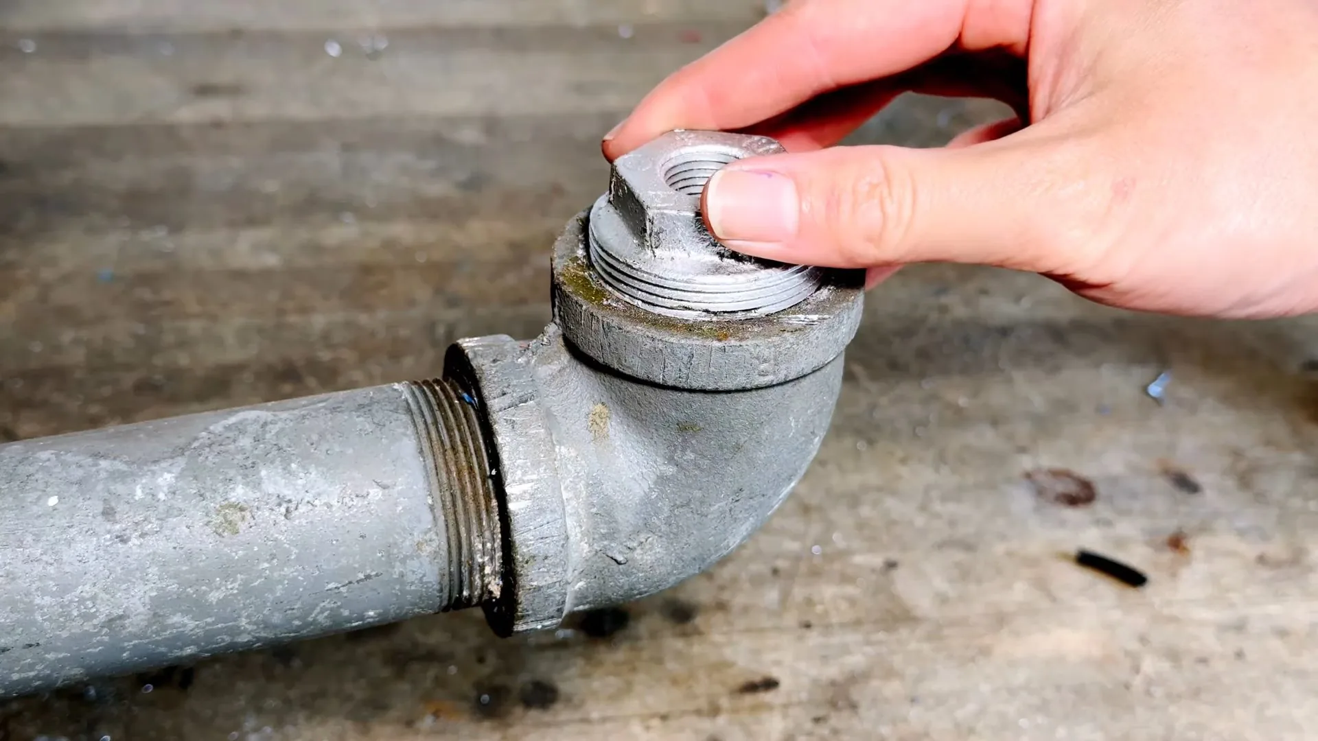 Hand unscrewing a cap from a grey galvanized steel pipe elbow