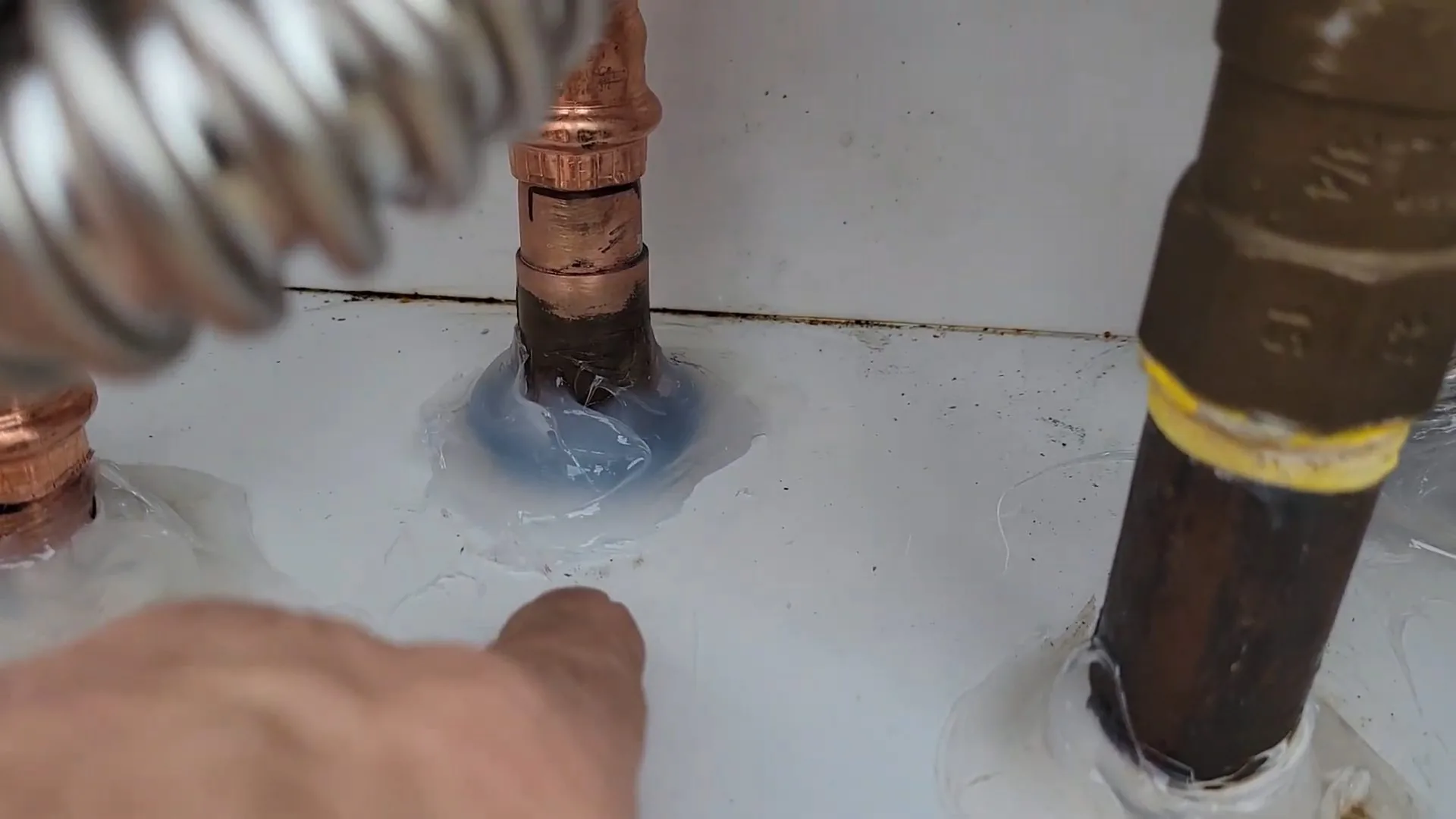 Close view of a flexible line and black gas pipe at the base of a tankless water heater