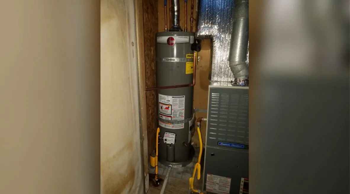 Gas water heater in a narrow cupboard beside a furnace with flue and water lines overhead