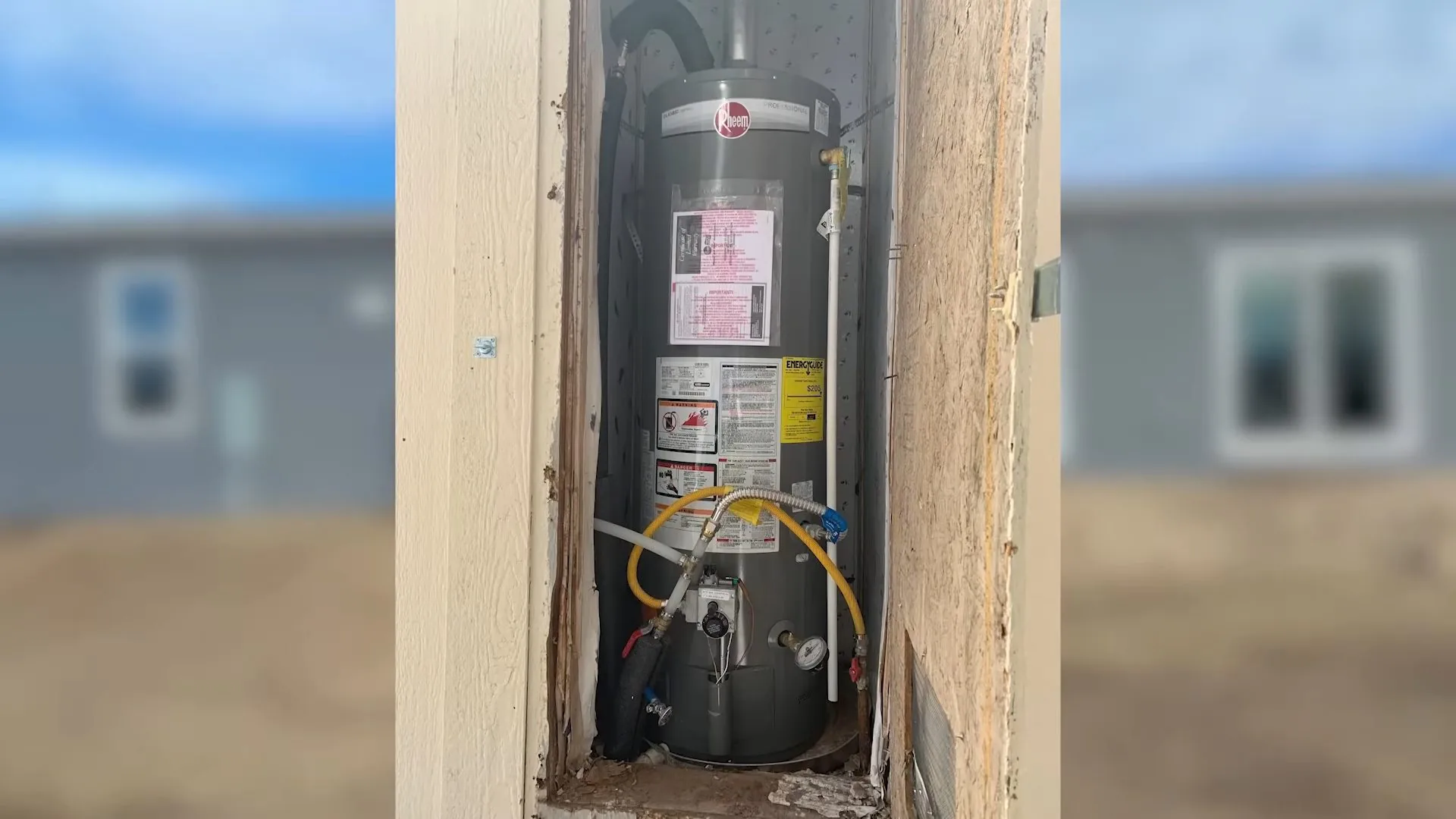 Gas water heater standing in an open framed enclosure with a yellow gas connector at its base