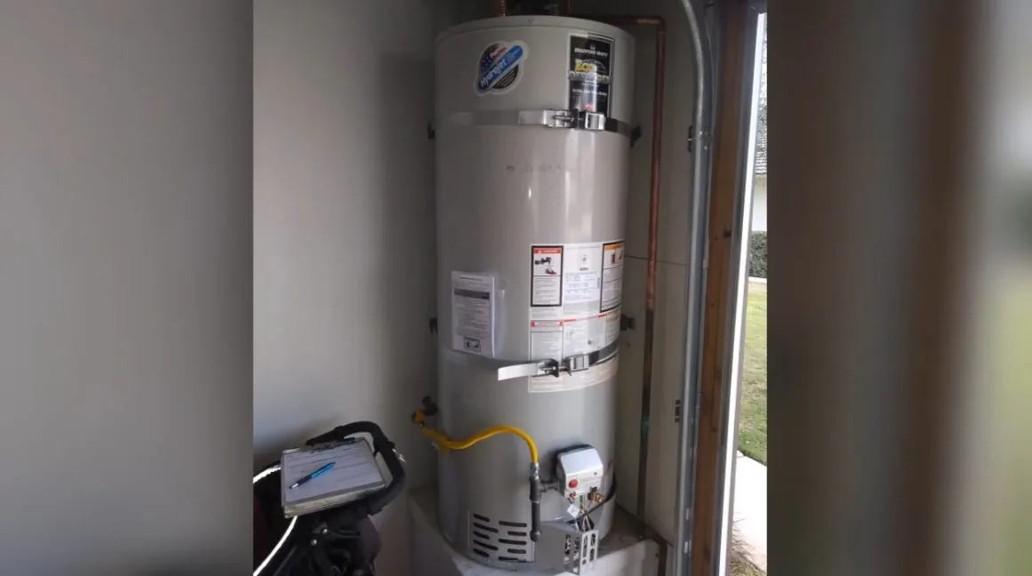 Gas water heater in a small garage closet beside an open door, with a clipboard on a cart in front