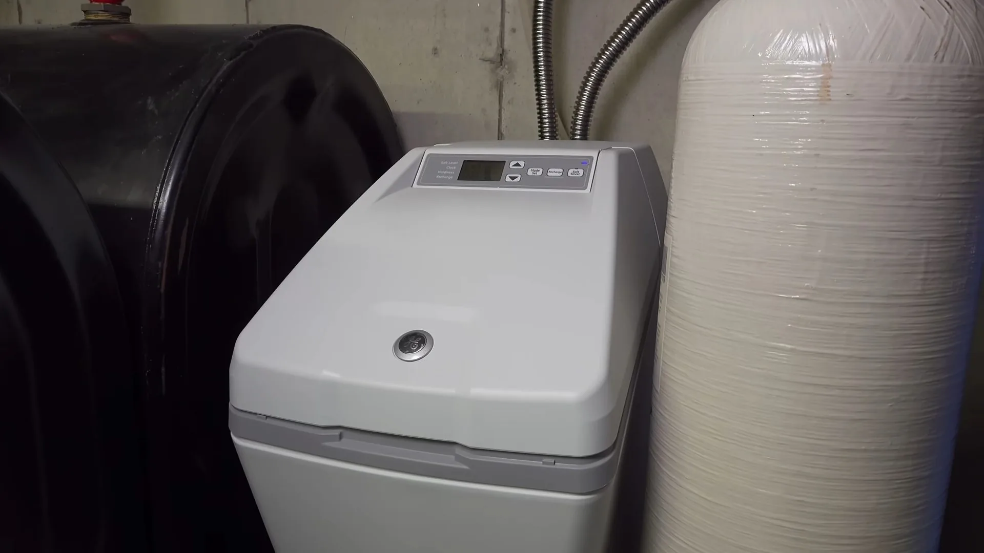 Grey softener cabinet beside a black brine tank and a white resin tank