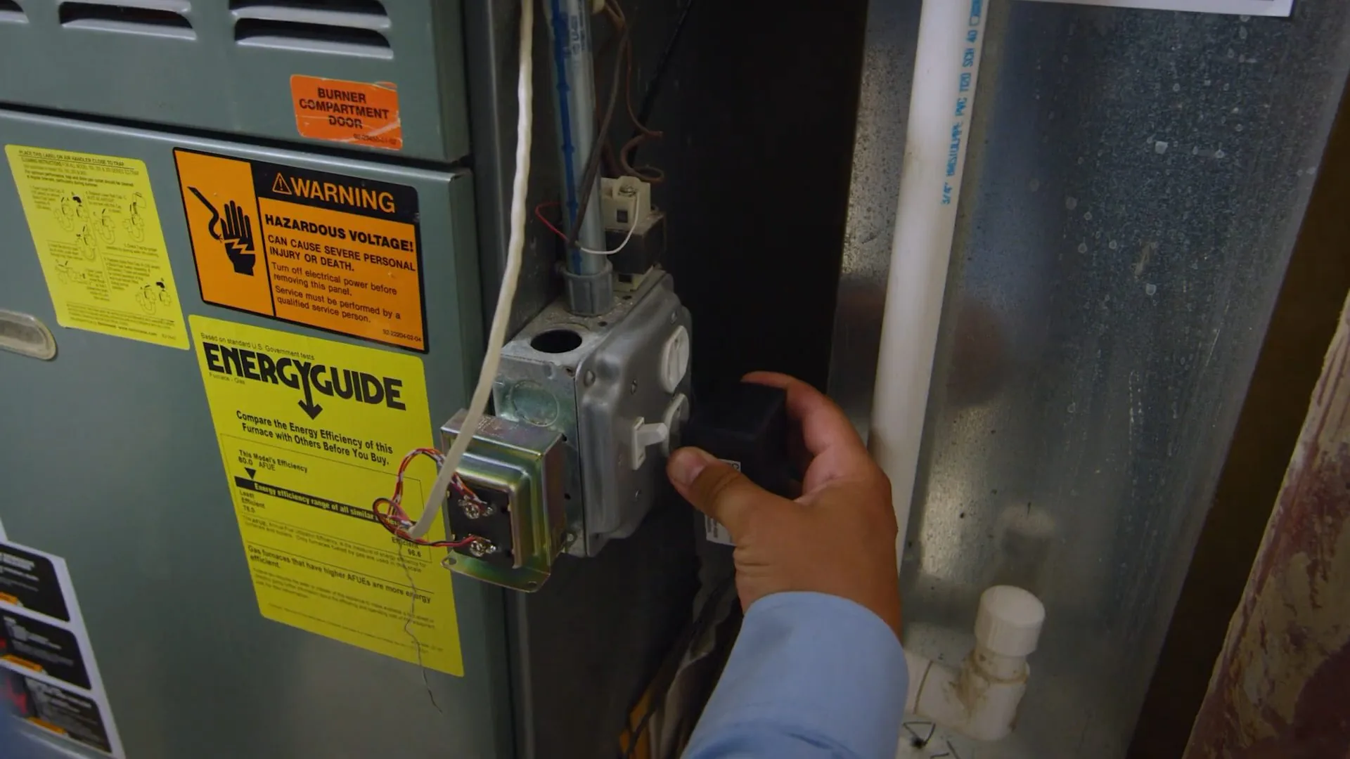 Hand reaching to the gas control of a heater with yellow warning labels beside it