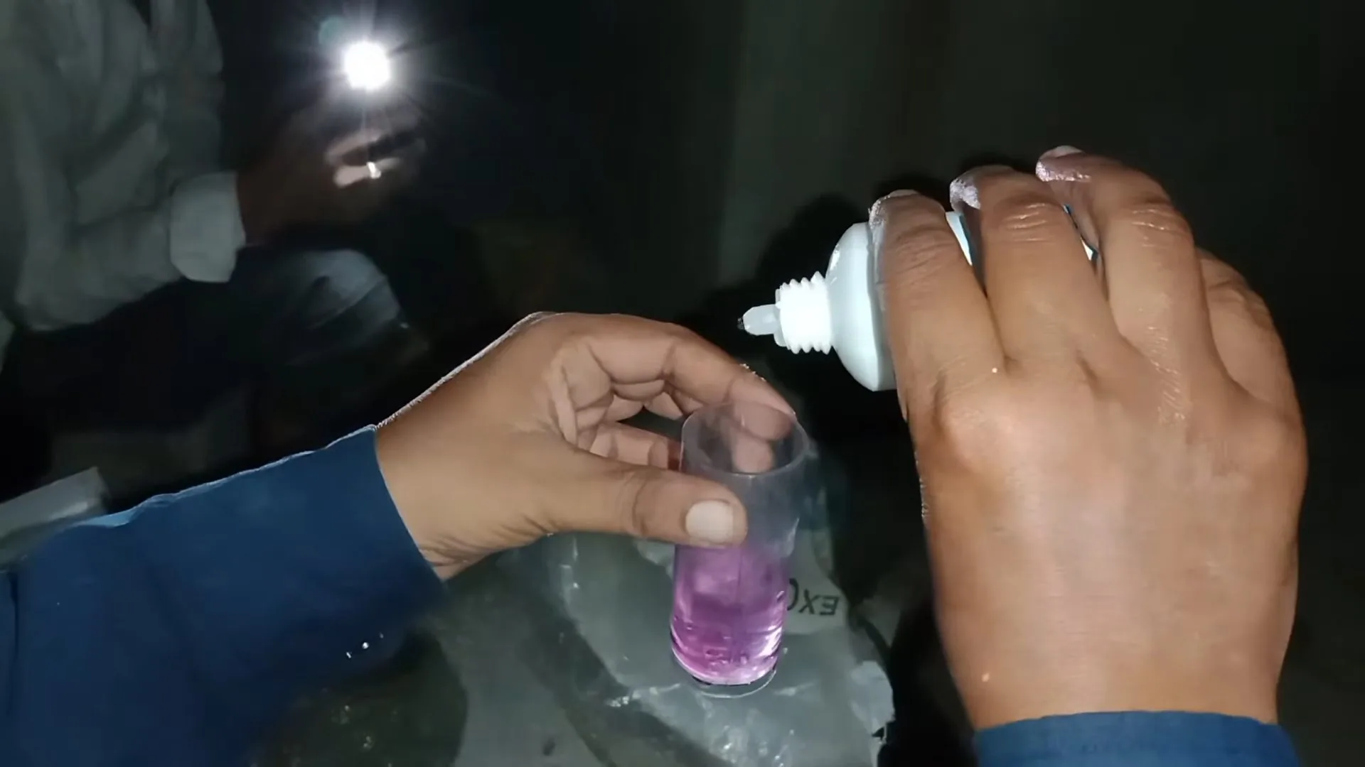 Hand dropping reagent into a glass of water, the water turning pink