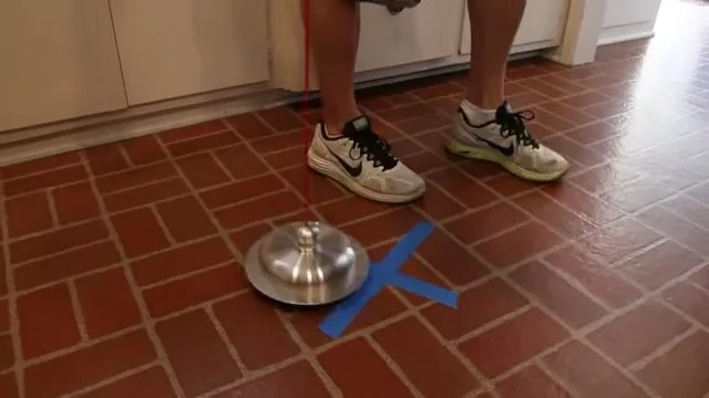 Metal listening disc on a brick-red tile floor with a blue tape X beside it