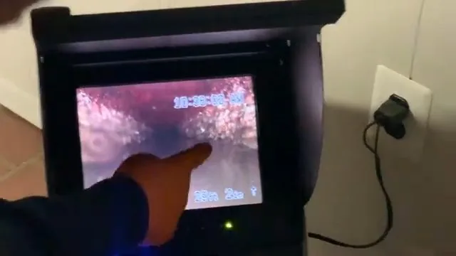 Hand pointing at a drain camera monitor showing the inside of a pipe