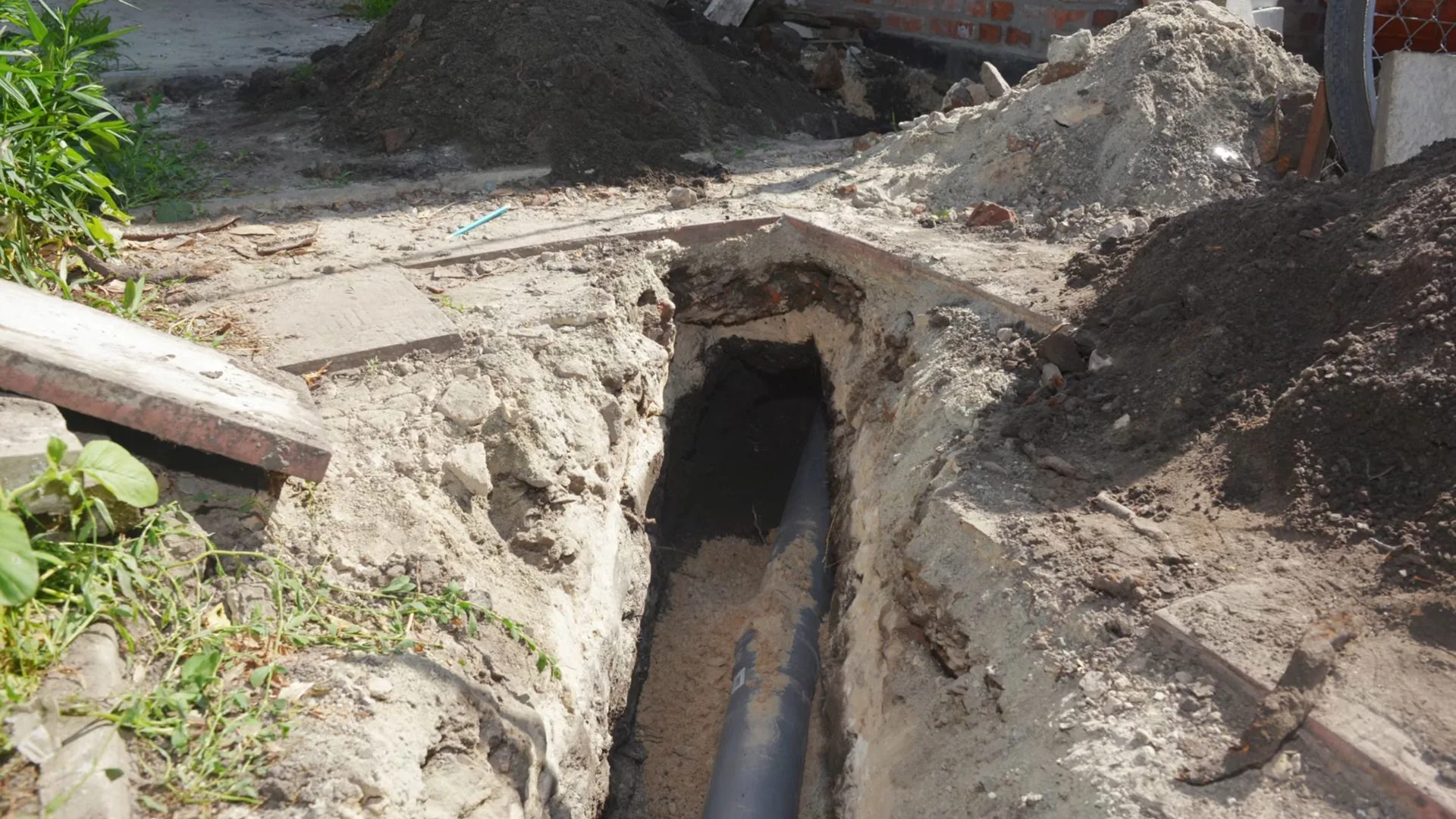 Open trench running along the side of a house with old pipe exposed in the bottom