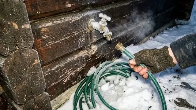 Outdoor tap on a timber wall with steam rising and a green hose lying in snow