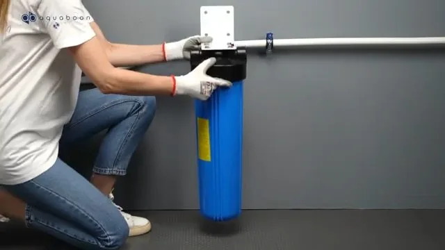 Person kneeling to fit a large blue filter housing against a wall bracket on white pipe