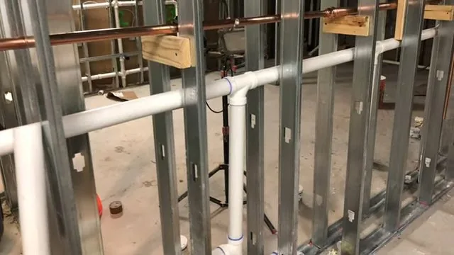 Steel stud wall with white PVC drain lines and copper supply pipe fitted between the studs before boarding