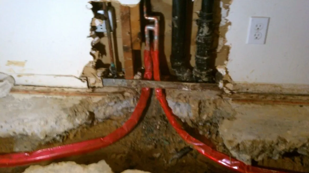 Red PEX supply lines running through a channel cut in a floor