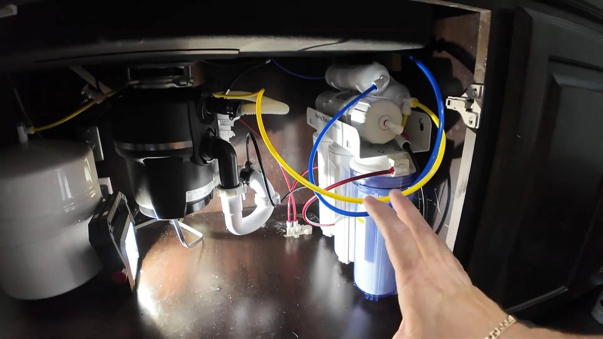 Reverse osmosis unit with coloured tubing mounted beneath a kitchen sink beside a disposal