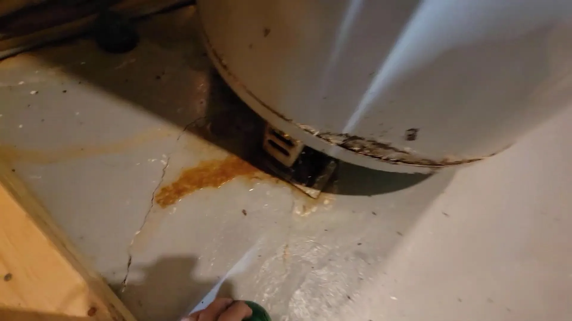 Rust stain and wet patch on the floor around the base of an old water heater tank