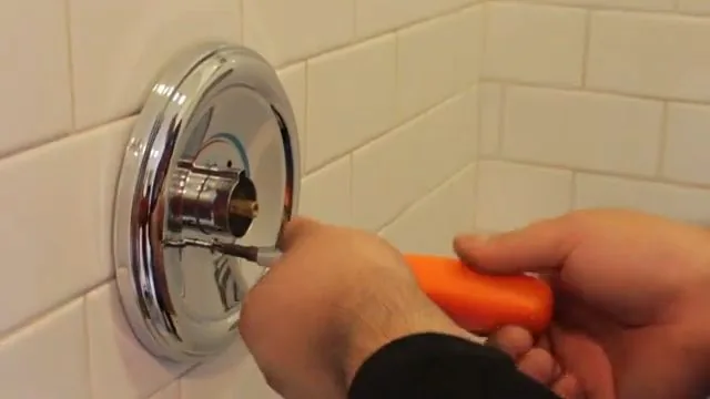 Chrome trim plate removed from a tiled shower wall with a screwdriver held beside it