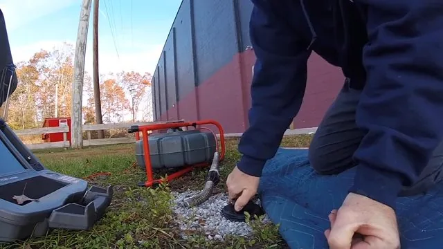Technician kneeling at a cleanout in gravel with a camera reel and monitor case beside him