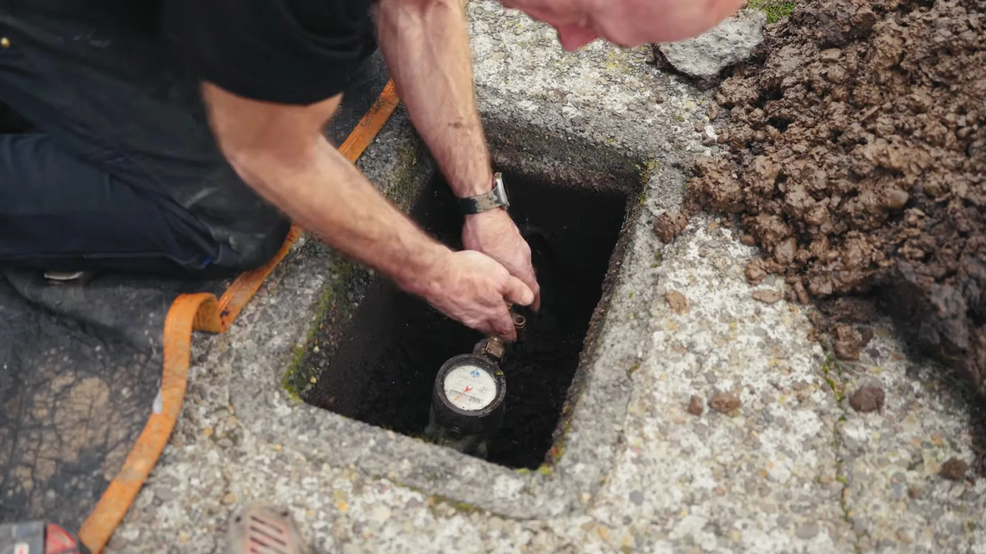 Technician reaching into a concrete meter box where a water meter dial is visible