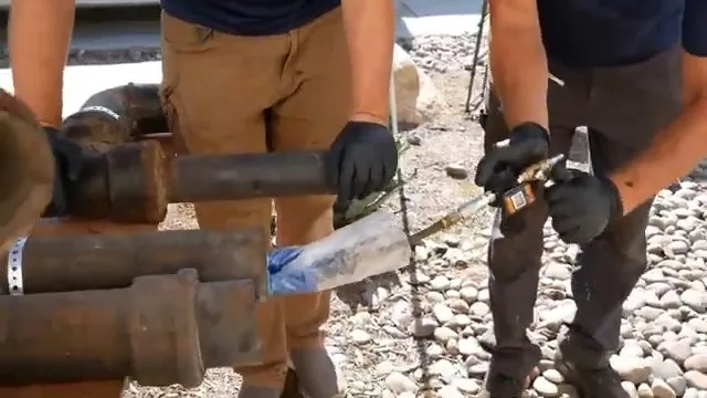 Two technicians feeding a blue liner sleeve into sections of old iron pipe