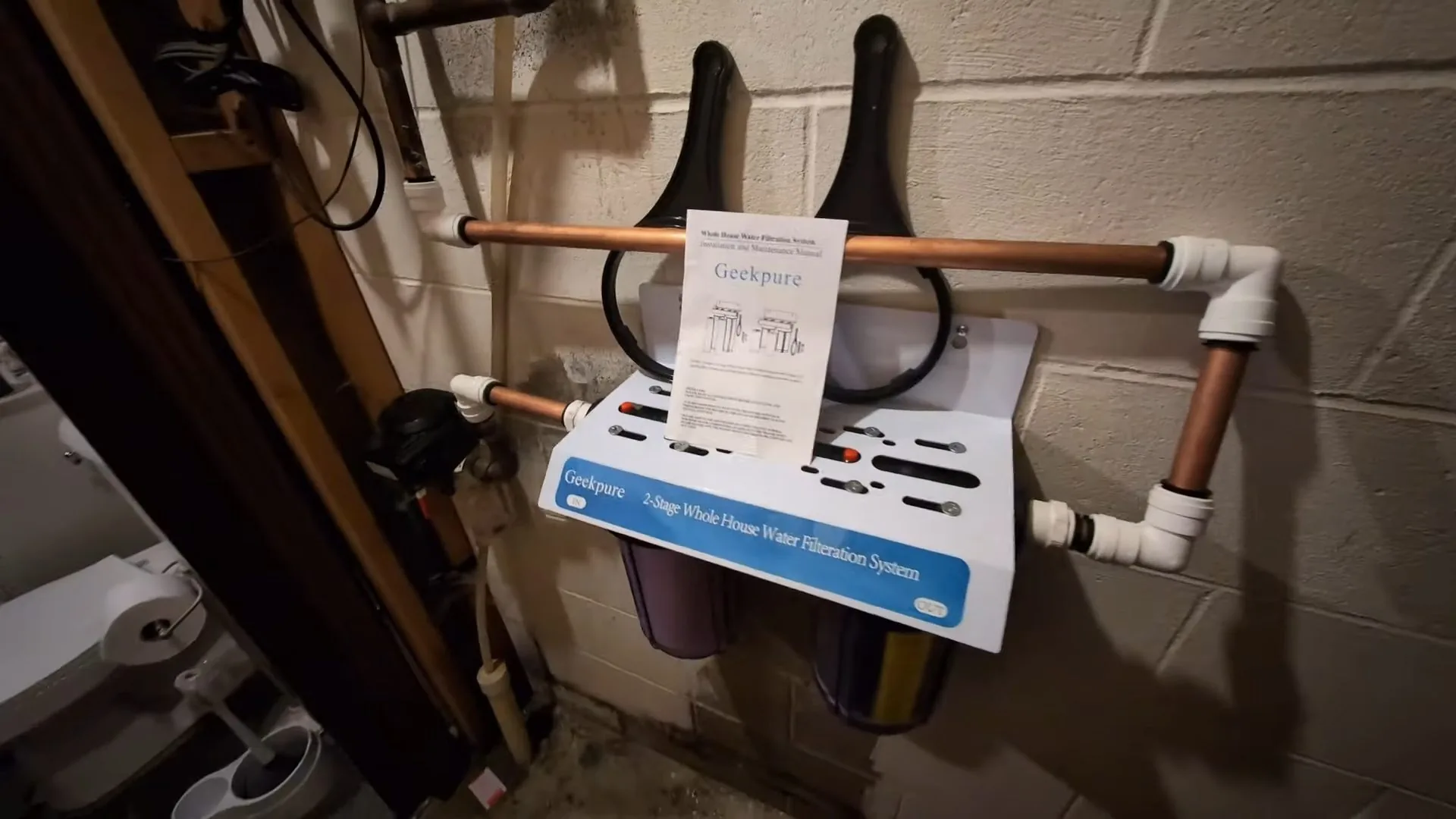 Two-stage whole-house filter mounted on a block basement wall with copper and PVC pipes