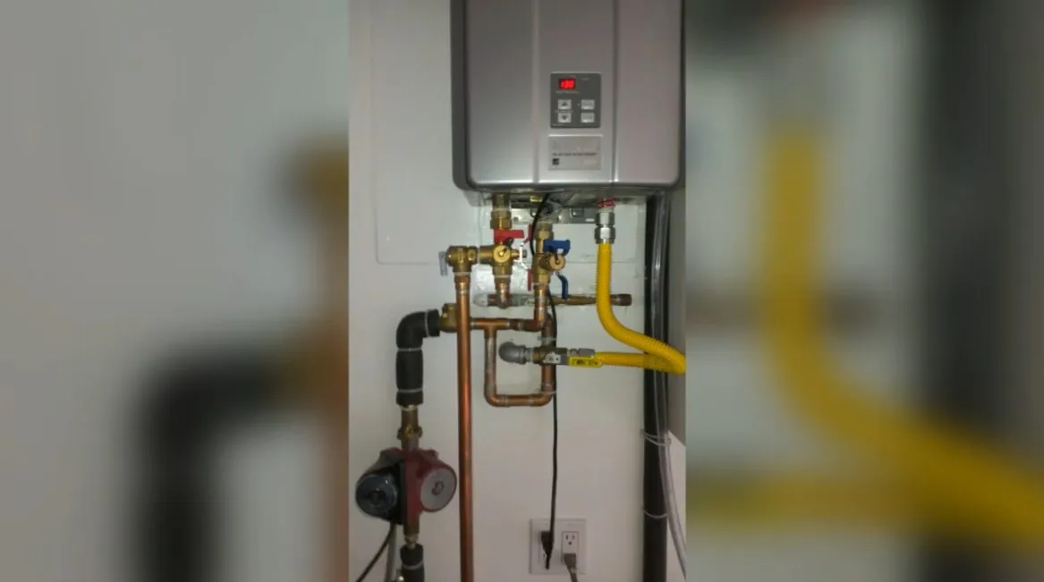 Wall-mounted tankless water heater with a yellow gas line and brass valves below it