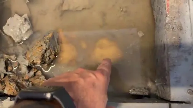 Hand pointing at water pooled in a hole broken through a concrete slab