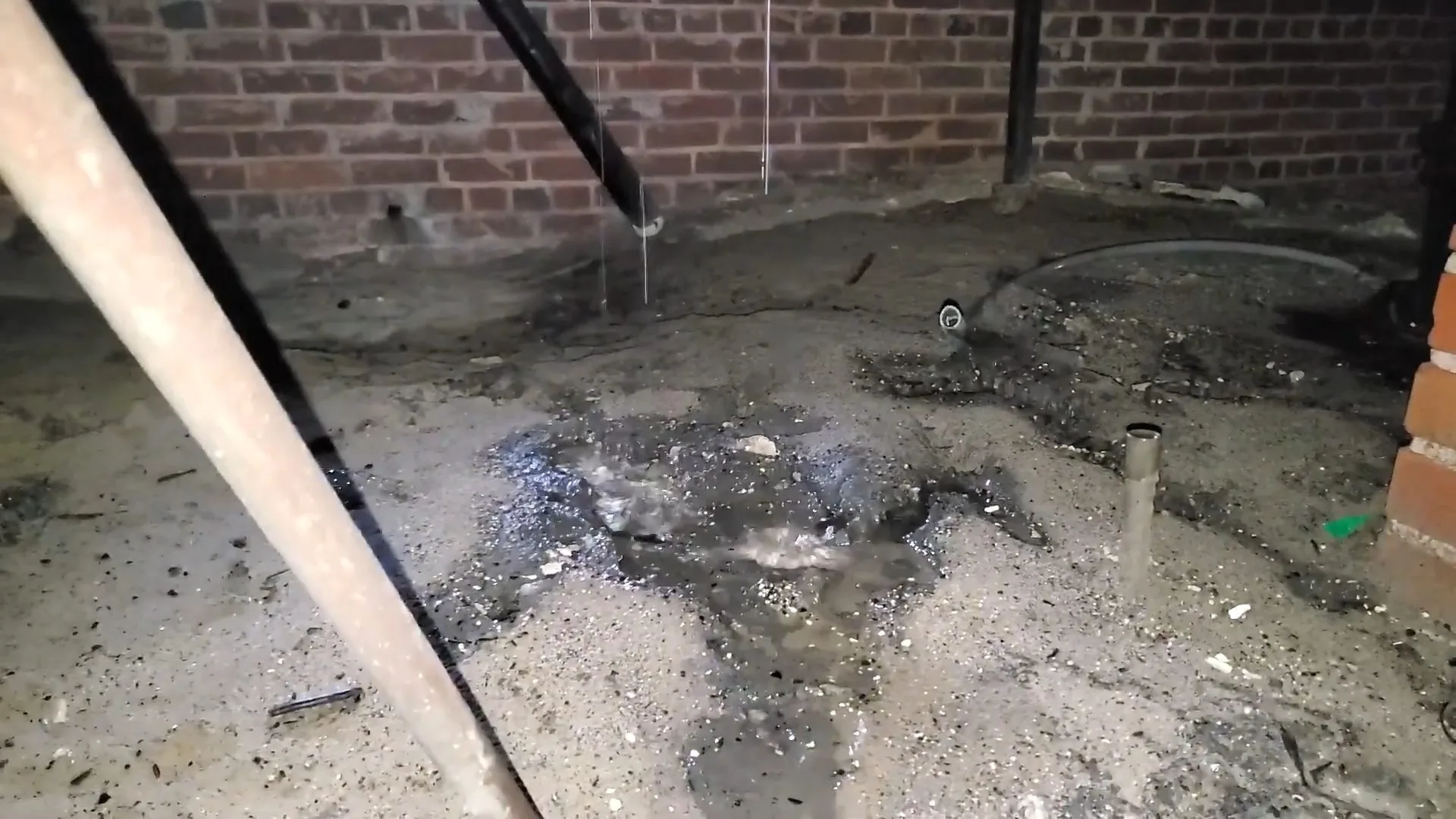 Dark wet ground below a leaking pipe in a brick-walled crawlspace
